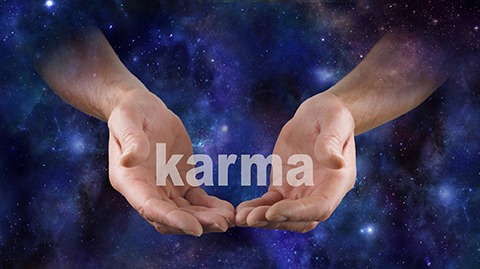 Two hands holding the word karma with a cosmic background - The Twelve Laws of Karma - Miller on the Money